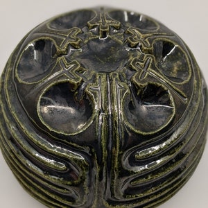 May include: A dark green ceramic bowl with intricate raised designs. The bowl has a rounded shape and a smooth, glossy finish.