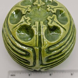 May include: A green ceramic sphere with a raised, intricate design. The sphere has a smooth, glossy finish and appears to be handmade.