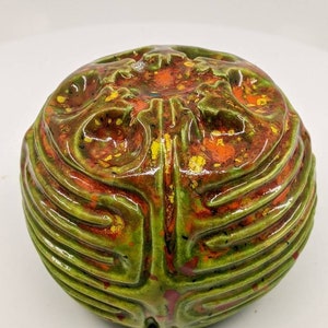 May include: A green ceramic sphere with a textured surface and red and yellow paint splatters.