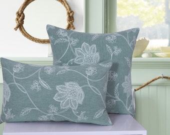 May include: Two decorative throw pillows with a floral pattern. The pillows are a light blue color with white floral designs. The pillows are on a white surface.