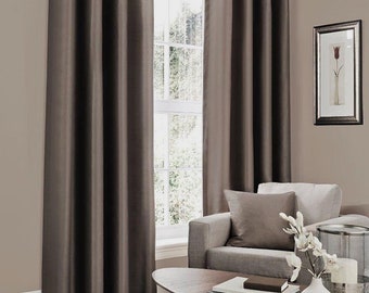 May include: A pair of brown blackout curtains with silver grommets hanging in a living room with a couch and coffee table. The curtains are closed and the room is lit by natural light.