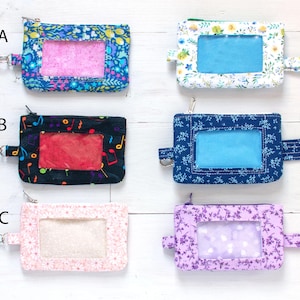 May include: Six fabric ID badge holders with clear windows and lanyards. The holders feature various patterns, including floral, musical notes, and solid colors. Each holder has a zipper closure and a matching lanyard for easy wear.