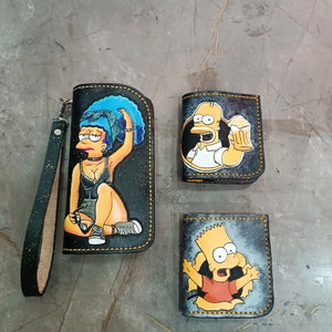 May include: A collection of hand-painted leather wallets featuring characters from The Simpsons. The wallets include a long clutch with a wrist strap, a small bi-fold wallet, and a cardholder, all with unique character designs and yellow stitching.