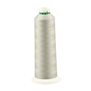 May include: A spool of silver gray thread with the word "MADERA" printed on the label.