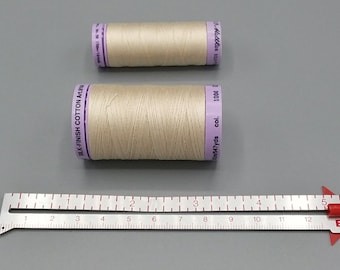 May include: Two spools of white thread, one larger than the other, with purple labels that read "SILK-FINISH COTTON Art" and "Mettler 150/1608 547yds col. 1000". A metal ruler with red markings is in the bottom of the image.