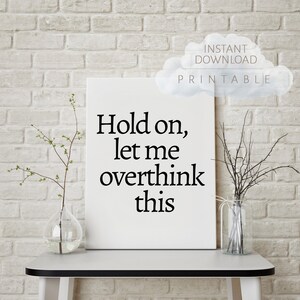 May include: White canvas print with black text that reads "Hold on, let me overthink this". The print is sitting on a white table with two clear glass vases, one with branches and the other with dried twigs.