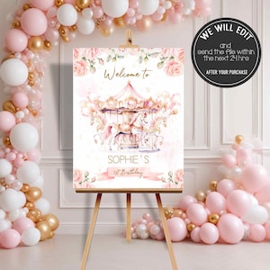 May include: A pink and gold welcome sign with a carousel illustration and the text "Welcome to Sophie's 1st Birthday". The sign is on an easel and surrounded by pink and gold balloons.