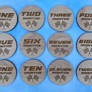 K&ouml;nnte beinhalten: Zw&ouml;lf Holz Kreise mit einem Rennflaggen-Design und den Zahlen eins bis zw&ouml;lf mit dem Wort "Monate" unter jeder Zahl.