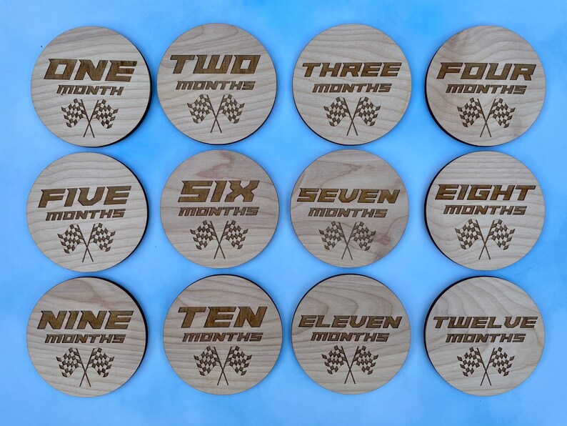 K&ouml;nnte beinhalten: Zw&ouml;lf Holz Kreise mit einem Rennflaggen-Design und den Zahlen eins bis zw&ouml;lf mit dem Wort "Monate" unter jeder Zahl.