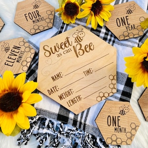 May include: Wooden hexagonal baby milestone signs with a bee theme. The signs feature a bee illustration and the text "Sweet as can Bee". The signs are decorated with honeycomb patterns and are perfect for capturing a baby's growth milestones.