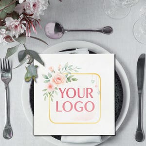 Może przedstawiać: Kwadratowa biała serwetka z kwiatowym wzorem i różowym napisem "YOUR LOGO", umieszczona na białym talerzu ze sztućcami. Kwiatowy wzór zawiera różowe róże i zielone liście ze złotą obwódką.