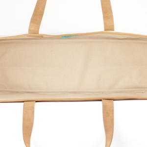 An empty tote bag with a tan interior and a brown exterior, featuring a handle and straps.