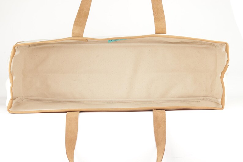 An empty tote bag with a tan interior and a brown exterior, featuring a handle and straps.