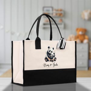 May include: A canvas tote bag with a black and white panda bear graphic hugging a baby panda. The bag has black handles and a black bottom panel. The text "Mary & Linda" is printed below the panda graphic.