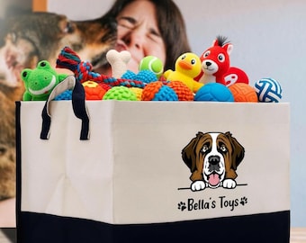 May include: A canvas storage bin with a black base and handles, filled with various dog toys. The bin features a Saint Bernard graphic and the text "Bella's Toys". Toys include a green frog, a yellow duck, and several balls.