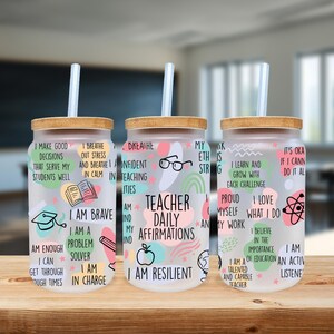 May include: Three glass tumblers with bamboo lids and straws. Each tumbler features a frosted design with colorful graphics and text, including affirmations for teachers. The text includes phrases like "I am brave" and "I am resilient."
