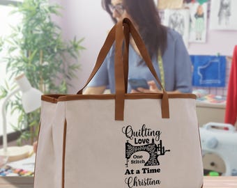 Peut inclure: Un sac fourre-tout beige avec des bordures et des poignées marron. Le sac porte l'inscription "Quilting Love, One Stitch At a Time, Christina" et un motif de machine à coudre noir. Le sac est posé sur une surface en bois.