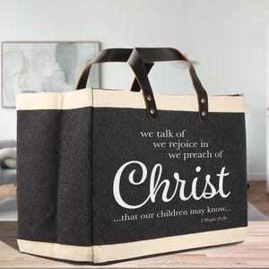 May include: A black and cream tote bag with leather handles. The bag features the word "Christ" in a stylized white font, along with the text "we talk of, we rejoice in, we preach of...that our children may know..." from 2 Nephi 25:26.