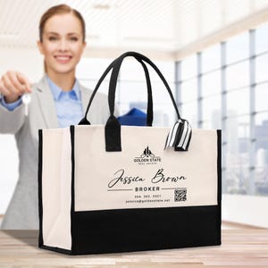 Op de afbeelding: Crème en zwarte draagtas met zwarte handvatten. De tas heeft de tekst "Golden State Real Estate" en "Jessica Brown, Broker". Een QR-code en contactgegevens worden ook weergegeven. De tas heeft een zwart-wit gestreept lint.