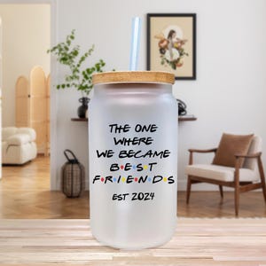 Op de afbeelding: Matte glazen beker met een bamboe deksel en een herbruikbaar rietje. De beker heeft de tekst "THE ONE WHERE WE BECAME BEST FRIENDS EST 2024" in zwart, met het woord "FRIENDS" in regenboogkleuren.