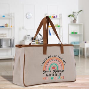 Op de afbeelding: Beige draagtas met bruine rand en handvatten. De tas heeft een regenboogontwerp met de tekst "I teach kids to talk back" en "Speech Language Pathologist Mrs. Williams".