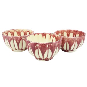 May include: Three small white ceramic bowls with a red and white floral design. The bowls are slightly scalloped at the rim.