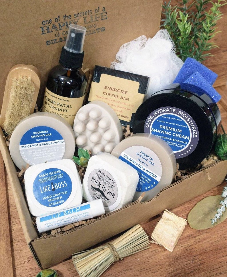May include: A gift box filled with various men's grooming products, including a shaving cream, shaving bar, shower steamer, lip balm, and aftershave. The box is made of brown cardboard and has a white label with the text "one of the secrets of a HAPPY LIFE is to EAT" on the front.