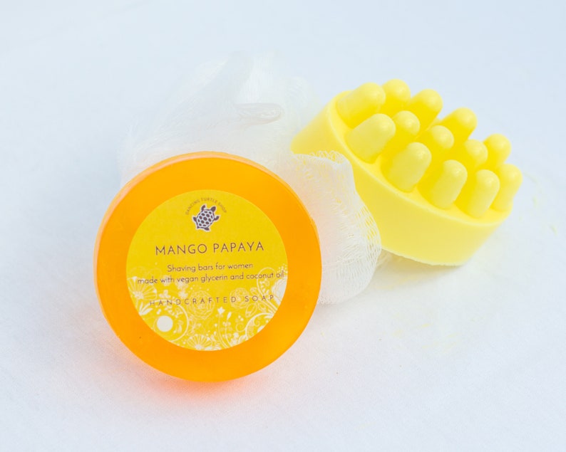 以下が含まれることがあります： 黄色い石鹸が2つ。1つは丸型で、「MANGO PAPAYA 女性用シェービングバー  ビーガン グリセリンとココナッツオイル使用  手作り石鹸」とラベルが貼ってあり、もう1つは表面がざらざらしている。