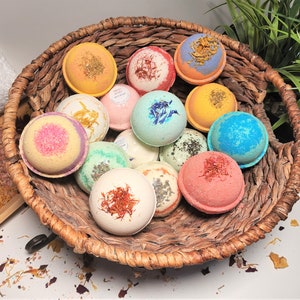 May include: A woven basket overflowing with colorful bath bombs. The bath bombs are round and decorated with dried herbs and flower petals. Colors include yellow, pink, blue, green, and red. A spa-like theme.