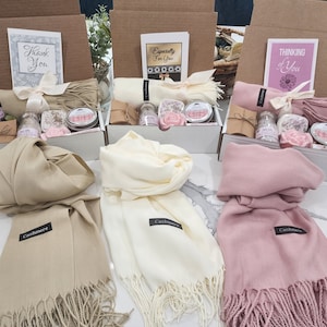May include: Three gift boxes with different coloured cashmere scarves, each box contains bath products and a card with a different message. The cards say "Thank You", "Especially For You", and "Thinking of You".