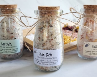 May include: Three glass jars with cork lids filled with bath salts. The jars are tied with twine and have labels with the names of the scents: Peppermint & Eucalyptus, Lavender & Chamomile, and Citrus & Ylang Ylang. The labels also list the ingredients, including Himalayan pink salt, Epsom salt, and essential oils.
