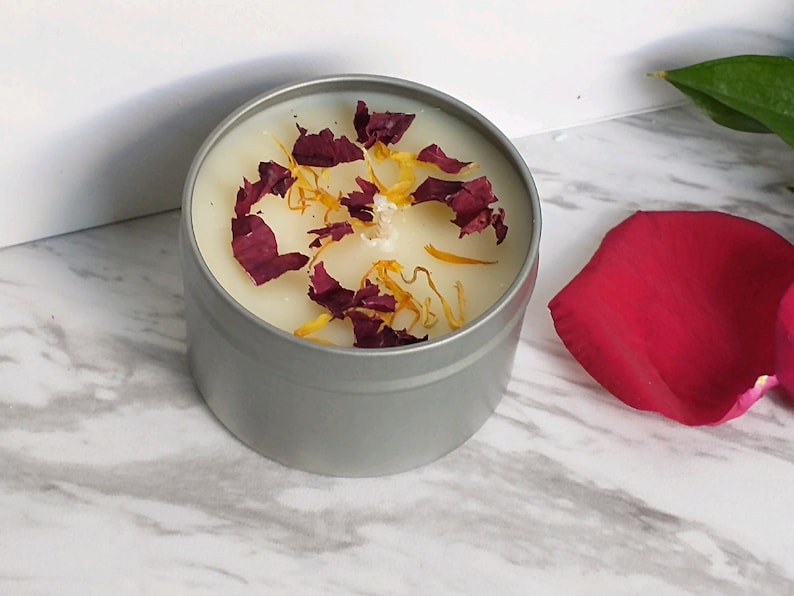 May include: A silver tin candle with a white wax top. The wax is decorated with dried red and yellow flower petals.