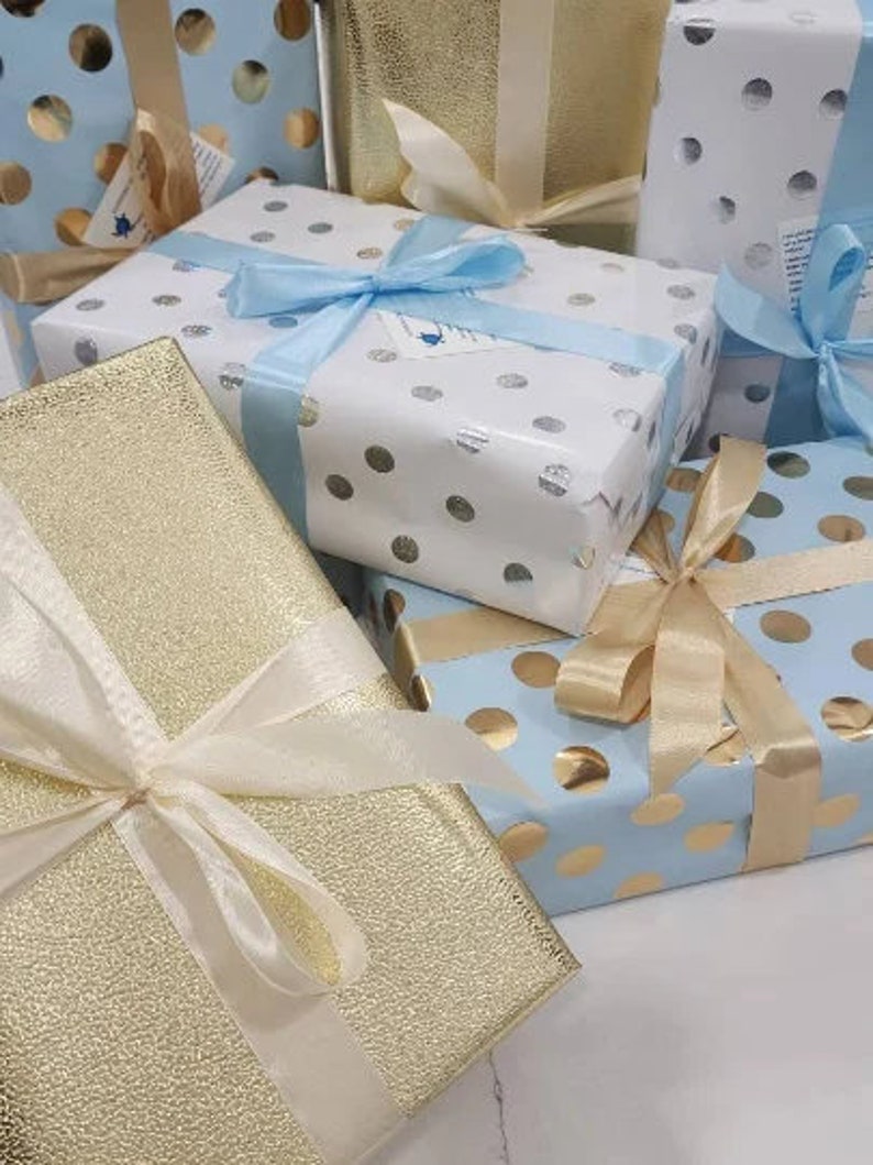 May include: A stack of gift boxes wrapped in blue and gold paper with white polka dots. The boxes are tied with white and blue ribbon.