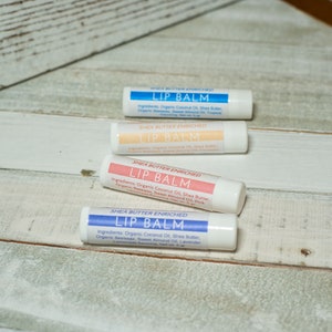 May include: Four shea butter enriched lip balms in white tubes with blue, pink, and peach labels. The labels read "Shea Butter Enriched Lip Balm" and list ingredients.