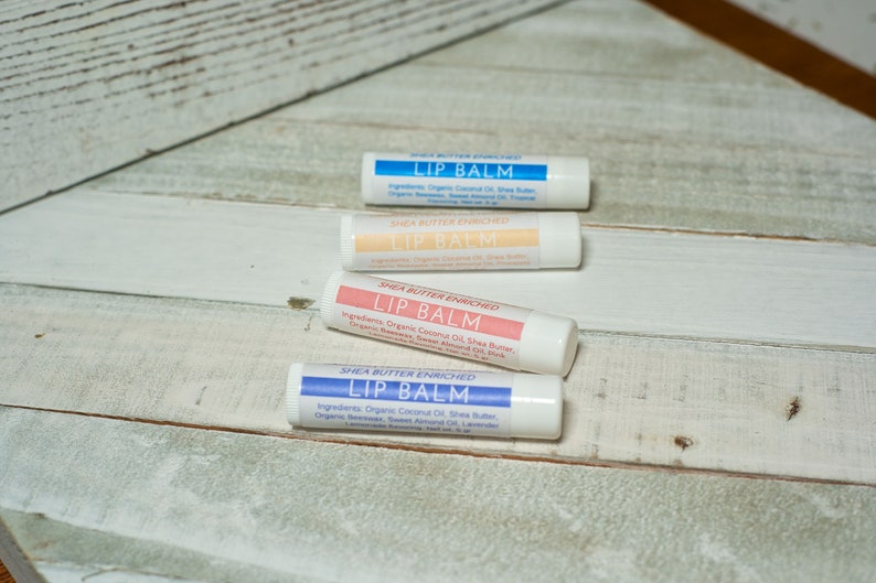 May include: Four shea butter enriched lip balms in white tubes with blue, pink, and peach labels. The labels read "Shea Butter Enriched Lip Balm" and list ingredients.