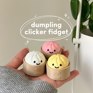 May include: Three colourful dumpling clicker fidget toys. One is white, one is pink, and one is yellow. Each dumpling has a smiling face and sits in a small, brown, bamboo-style container. The text "dumpling clicker fidget" is in a white oval.