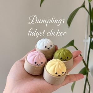 May include: Four colourful dumpling fidget clickers in a hand. The dumplings are white, pink, green, and yellow, each with a smiling face. The text "Dumplings fidget clicker" is in the background.