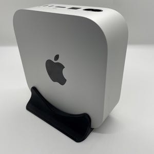 Könnte beinhalten: Ein weißer Apple Mac mini Computer mit einem schwarzen Apple-Logo auf der Vorderseite, der auf einem schwarzen Ständer steht.