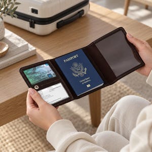 May include: A dark brown leather passport holder featuring a central slot for a United States passport, a clear plastic window for an identification card, and an additional card slot. The interior is lined with dark brown stitching throughout.