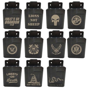 May include: A selection of black, rectangular items with different designs and text. Some display military emblems, a skull, and phrases such as "Let's Go Brandon," "Lions Not Sheep," and "Liberty or Death."