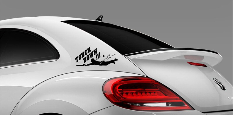 K&ouml;nnte beinhalten: Ein wei&szlig;es Auto mit einem schwarzen Vinyl-Aufkleber auf der Heckscheibe. Der Aufkleber lautet "Touch Down!!!" und zeigt eine Person, die ins Wasser springt.