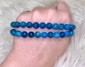 May include: Two blue gemstone bracelets with round beads. The bracelets are stacked on top of each other.