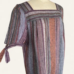 May include: A vintage-style dress with a square neckline and short sleeves. The dress features vertical stripes in shades of purple, brown, and gray. The sleeves are tied at the elbow. The dress is displayed on a mannequin.