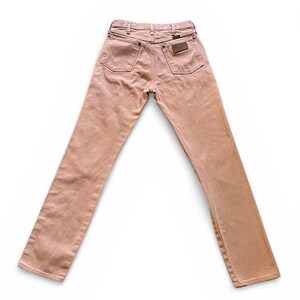 May include: A pair of light pink denim jeans featuring a high-rise waist, a classic five-pocket design, and a brown leather patch on the back right pocket. The jeans have a straight-leg cut with visible stitching and metal rivets throughout.