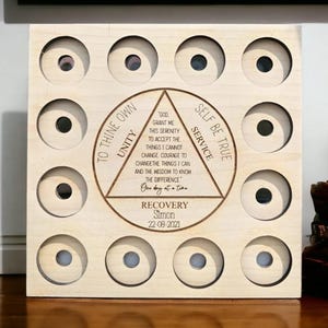 May include: A light-coloured wooden plaque with a grid of circular holes. The centre features a triangle with text, including "God grant me this serenity." The plaque is personalised with the name "Simon" and the date "22-08-2021."