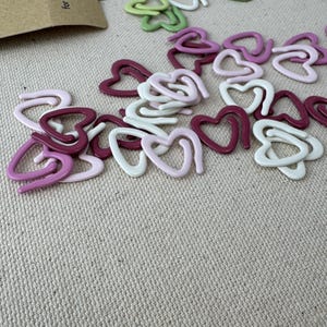 May include: Assortment of heart-shaped stitch markers in pink, white, and green. The markers are made of plastic and are designed for crochet and knitting.