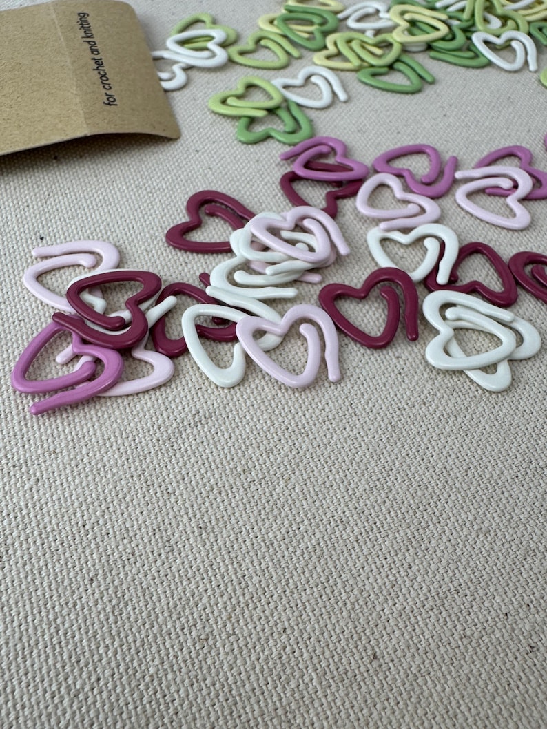 May include: Assortment of heart-shaped stitch markers in pink, white, and green. The markers are made of plastic and are designed for crochet and knitting.