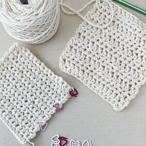 May include: Two crocheted squares made with cream colored yarn, a ball of cream colored yarn, a green crochet hook, and a pile of pink and red heart shaped stitch markers.