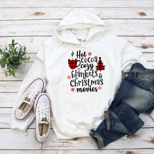 Puede incluir: Sudadera con capucha blanca con un diseño de cuadros rojos y negros de búfalo con el texto "Hot Cocoa Cozy Blankets & Christmas Movies".