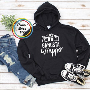 Puede incluir: Sudadera con capucha negra con texto blanco que dice "Gangsta Wrapper" y un gráfico de tres regalos envueltos.
